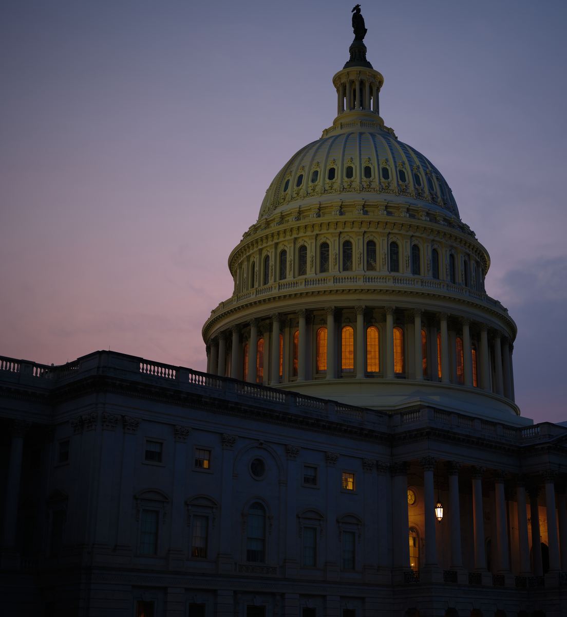 The Capitol dome at blue hour, its drum windows lit amber against a violet sky
